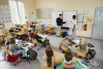 Male and female teachers solving maths problem in front of students in classroom