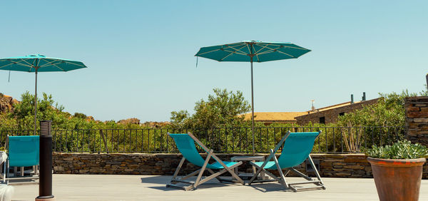 Chairs and tables by swimming pool against clear blue sky
