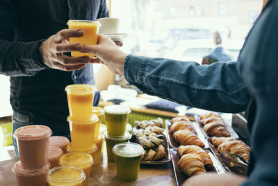 Midsection of owner serving juice to male customer in coffee shop