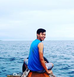 Young man sitting in sea against sky