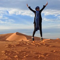 Excited woman jumping on sand in desert against sky