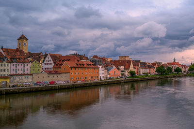 Buildings by river against cloudy sky