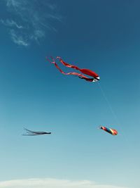 Low angle view of kites flying against blue sky