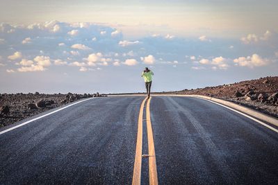 Full length of man walking on road against cloudy sky