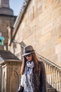 Young woman wearing hat standing against built structure in winter