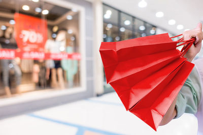 Midsection of man holding red shopping bags at mall