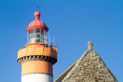 Low angle view of lighthouse by church against clear blue sky