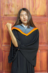 Portrait of beautiful young woman in graduation gown standing door