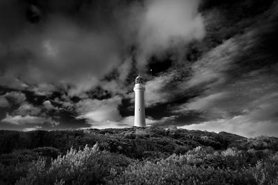 High contrast black and white view of lighthouse on field against dramatic cloudy sky