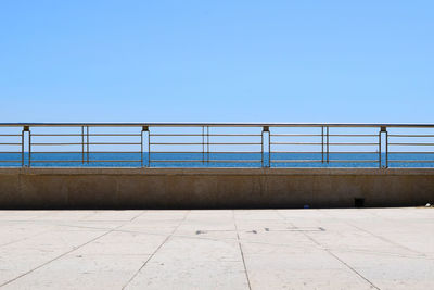 Empty pedestrian zone by sea against clear blue sky