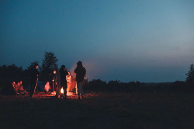 Silhouette people standing by campfire against clear sky at night