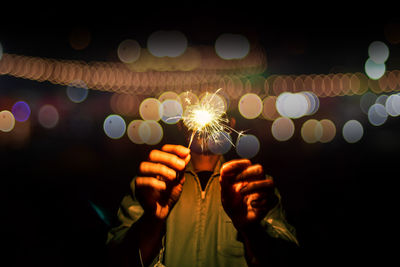 Midsection of man holding illuminated sparklers at night
