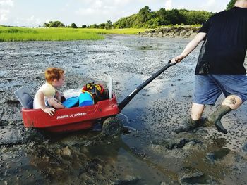 Man pulling son on cart in muddy lakeshore