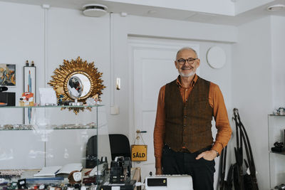 Portrait of smiling male owner with hand in pocket standing at store