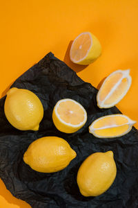 Group fresh lemons and pieces of slices on black matte crumpled clothespin tissue paper on yellow