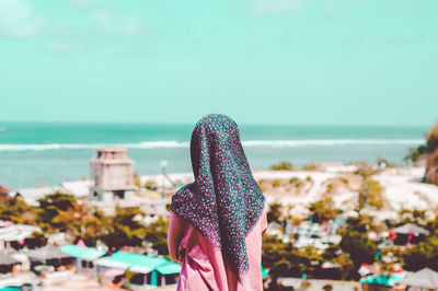 Rear view of woman wearing hijab looking at view while standing at beach