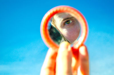 Cropped hand of woman holding sunglasses against blue sky