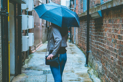 Woman holding umbrella while walking on street amidst buildings