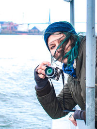 Portrait of young woman photographing with camera by sea