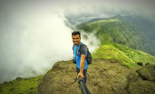 High angle view of young man taking selfie on mountain against clouds