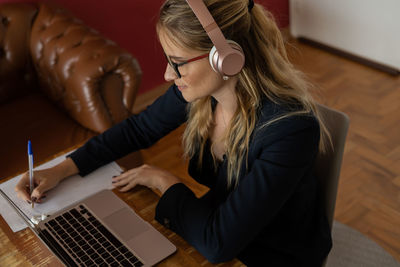 Woman working at home with laptop and papers on desk and headphones. home office . gray notebook 