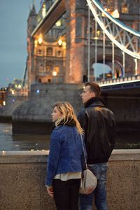 Rear view of couple looking away while standing by retaining wall at tower bridge