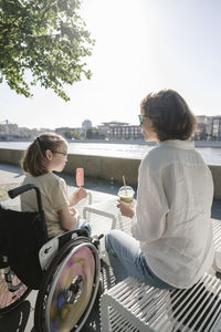 Mother and daughter sitting at park on sunny day