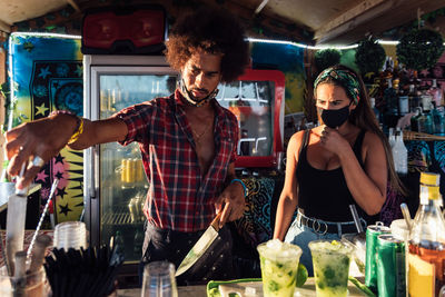 Adult ethnic man and woman standing at counter and preparing drinks for order while working together in outdoor bar