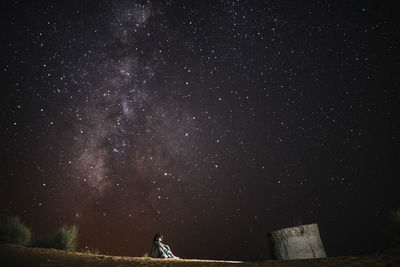Low angle view of woman sitting on field against sky at night