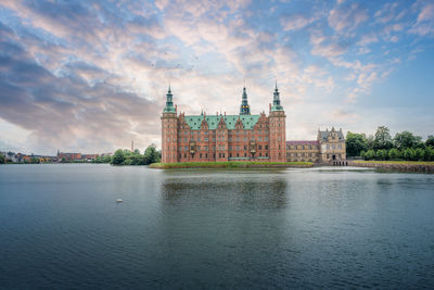 Buildings by river against cloudy sky