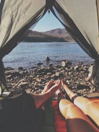 Low section of couple relaxing in tent at lakeshore