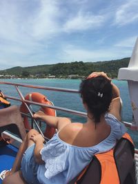 Rear view of woman sitting on boat in sea against sky