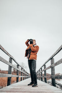Man photographing on footbridge against clear sky
