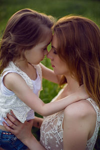 Mom and daughter are sitting in a green field in white t-shirt