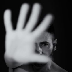 Close-up portrait of man gesturing stop sign against black background