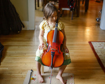 Above-view of cute barefoot child in window light holding a tiny cello