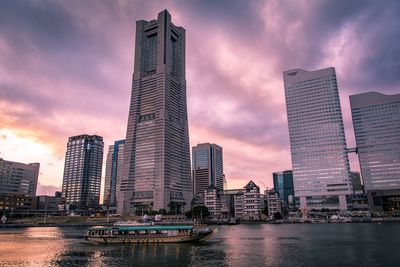 Modern buildings by river against sky during sunset