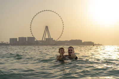 Rear view of woman swimming in sea against sky during sunset