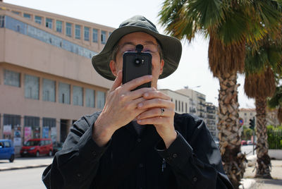 Man photographing with mobile phone while standing in city