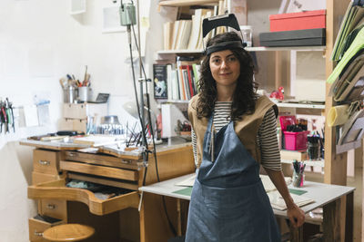 Portrait of confident female artisan standing by table in workshop