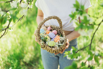 Funny teen girl with eggs basket and bunny ears on easter egg hunt in sunny spring garden