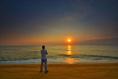 Rear view of man standing on beach during sunset