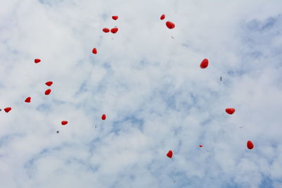 Low angle view of red heart shaped helium balloons flying in cloudy sky