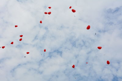 Low angle view of hot air balloons flying against cloudy sky