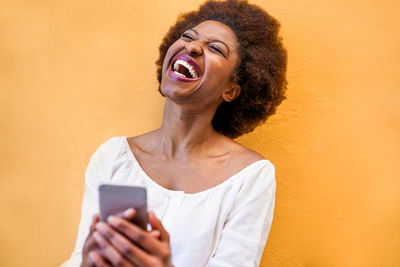 Cheerful woman holding mobile phone against orange wall