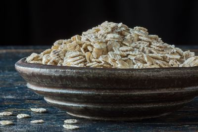 Close-up of barley flakes in bowl on table against black background