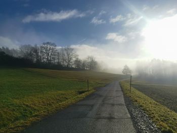 Empty road amidst field against sky