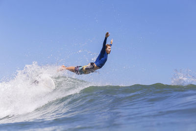 Side view of male surfer jumping on sea against clear blue sky