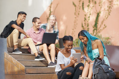 Young friends using laptop and tablet sitting on steps