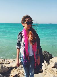 Young woman standing on rocks by sea against clear sky